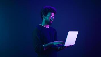 Arabian Indian man guy male programmer coder internet computer developer businessman business guy gamer hold laptop computer invite come here welcome nod head invitation work in violet neon background photo