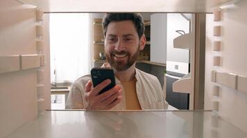 Hungry man guy open empty refrigerator poor crisis order food delivery with smartphone online buying products ordering goods with mobile phone store cellphone app point of view POV from inside fridge photo