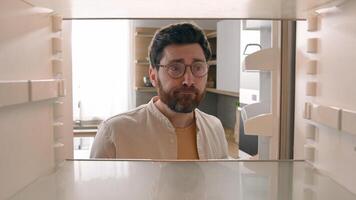 Hungry Caucasian bachelor man looking for food in empty fridge finding no meal products feeling sad disappointed poor unemployment need delivery service POV point of view from inside refrigerator photo