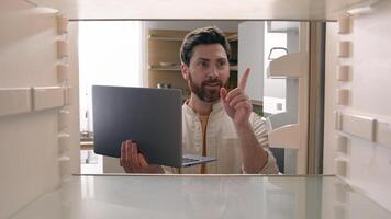 Hungry man guy open empty refrigerator confused find problem solution idea order food delivery laptop online buying products ordering goods with computer store app point of view POV from inside fridge photo