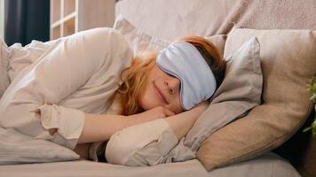 Sleepy beautiful woman waking up lying in comfortable white bed peeks out from under sleep mask opens eye happy smile fall asleep again girl female early good morning napping in cozy bedroom lazy lady photo