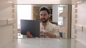 Hungry man guy open empty refrigerator confused find problem solution idea order food delivery laptop online buying products ordering goods with computer store app point of view POV from inside fridge photo