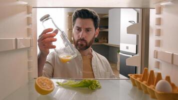 Man open empty refrigerator with half lemon lettuce leaf one egg slice of bread leftover orange juice in bottle find solution order food delivery with mobile phone app point of view from inside fridge photo