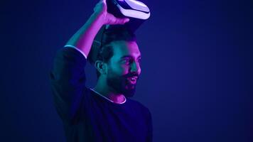 Arabian man take off VR glasses excited smile amazed with metaverse virtual reality cyberspace Indian guy with 3d goggles helmet happy wow reaction after play game meta universe neon ultraviolet space photo