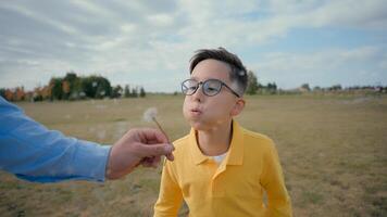Happy smiling joyful Caucasian child little boy kid having fun blowing dandelion air unrecognizable parent hand hold flower play outside field country meadow. Ecology nature environmental care village photo