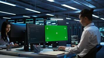 Engineer working with chroma key PC in data center used for managing gear energy consumption. Employee using isolated screen monitor in workspace used for automation in server farm, camera B photo