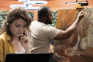 Woman searching for online inspiration while man is painting a masterpiece on canvas, doing research to find a model for their artwork. Team of artist collaborating on a painting. photo