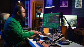 Producer composing new track with electronic gear in his home studio, creating music on mixing console and software interface. Talented artist songwriter controls panel to produce sounds. Camera B. photo