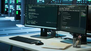 Data center workplace with networking systems installed used for managing rigs. Computer displays on desk in server farm used for overseeing equipment, handheld camera shot photo