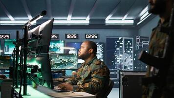 Army expert working in governmental facility operating surveillance tech, evaluating target data. Soldier doing job in HQ base of operations, engage enemy forces, camera B photo