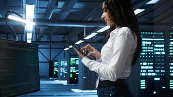 Data center computer scientist designing, implementing and managing infrastructure to ensure optimal performance and reliability. Woman in server room coding on tablet, camera B photo