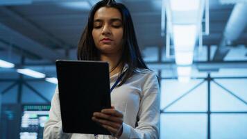 Software developer walking in data center, using tablet to design, implement and manage gear, ensuring optimal performance and reliability. IT worker in server farm coding on device, camera A photo