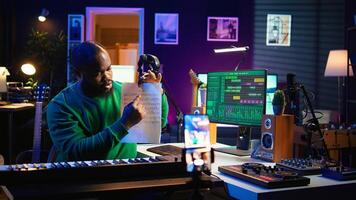 Skilled performer explaining sheet with musical notes on online tutorial, internet lessons in home studio. Producer artist teaching how to read acoustical notation, playing piano. Camera B. photo