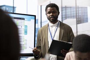 Financial expert briefing his team members about new enterprise objectives, showing analysis of their budget and expenses on interactive board. Resource allocation and project planning meeting. photo