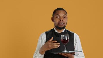 Waiter serving clients with a glass of red wine before dinner, recommending a special drink for customer satisfaction. Employee carrying a tray and serves people with professionalism. Camera A. photo