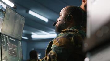 Military dispatcher using headphones microphone, offering information to commanders fighting on front lines. Army expert providing intel for troops in base of operations, camera A photo