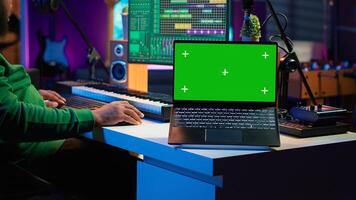 Producer editing his audio files and recordings on digital pc interface, sitting next to an isolated mockup screen. Sound engineer mixing and mastering songs with console in home studio. Camera A. photo