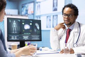 Physician reviewing MRI scan and x ray test results with a patient in medical office, explaining the diagnostics. Doctor pointing at analysis to discuss about the illness, medical technology. photo