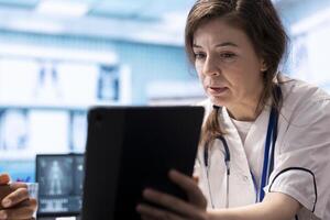 General practitioner presenting the test findings via scan interpretation on tablet, discussing about the diagnostic and possible treatment. Medical expert provides advice to patient. photo