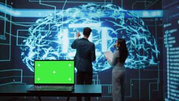 Teamworking AI technicians using green screen laptop for business data analysis. Team of IT experts works on mockup notebook to automatize tasks using artificial intelligence, camera B photo