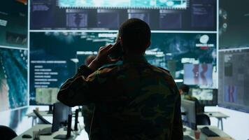 Military man answers phone call in a mission control center, working with advanced technology and satellite imagery to track potential threats and real time data. Intelligence activities. Camera B. photo