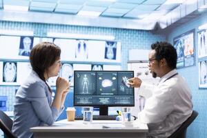 Medic expert showing the x ray imaging test results to patient at check up, discussing about treatment and medical advice. Doctor pointing at radiography scans for interpretation, diagnostic report. photo