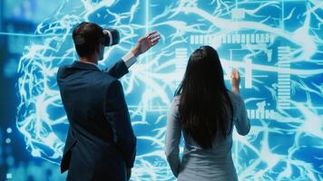 Engineer wearing VR headset looking at hologram of artificial intelligence human brain simulation, assisted by colleague. IT specialist and coworker interacting with AI visualization, camera A photo