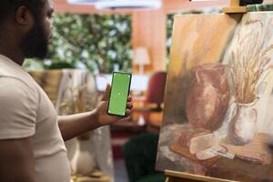 African american painter using a gadget with copy space screen in workshop, working on his new nature inspired masterpiece on canvas. Using watercolor paint and creativity in atelier. photo