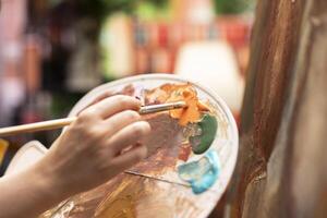 Talented artist painting an artwork with colorful paints mixed on a palette, creating a beautiful creative paintwork with a painting technique in her atelier. Painter mixing watercolor. Close up. photo