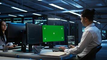 Engineer in data center monitoring security threats using mockup computer, implementing cybersecurity measures. Man using green screen PC, ensuring compliance with regulations, camera B photo