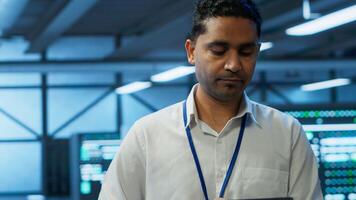 Engineer walking in data center, monitoring security threats, implementing cybersecurity measures. Indian man ensuring compliance with regulations to protect data center gear, camera A photo
