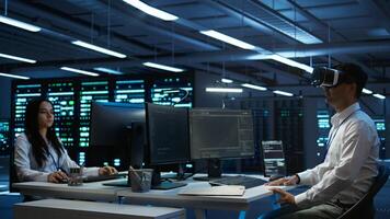 Admin in data center using virtual reality tech to ensure system can handle networking tasks. Server room worker wearing VR headset to track network traffic with PC, making improvements, camera B photo