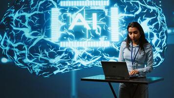 Technician in high tech workspace managing call center tasks, speaking into headset while doing monitoring with laptop. AI company employee talking with clients through headphones mic, camera A photo