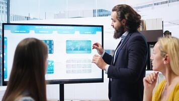 Team leader in company financial department showing stock portfolio on big screen containing collection of investment assets. Businessman showing stock demand surge in large display, camera A photo