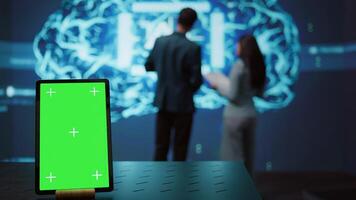 Green screen tablet used by computer scientists in startup doing advancements in AI field. Employees working on mockup device in workspace featuring artificial intelligence systems, camera B photo
