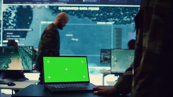Commander examines a greenscreen on laptop in military command center, reconnaissance army division. Operator gathering intelligence from the field, transmitting real time data. Camera B. photo