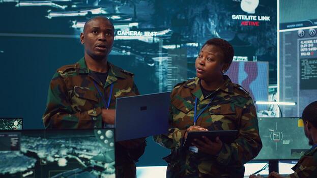 Sergeant major and female soldier checking real time field data in command post monitoring room, examining missions and operations. Team of troops interprets satellite imagery. Camera A. photo