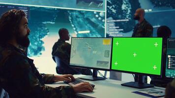 Army officer uses satellite radar footage and a greenscreen in military command post, working to gather intelligence and detect enemy ships. Commander operator at government agency. Camera B. photo