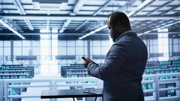 System administrator in server room establishment installing newly ordered storage unit. Software developer working in data center facility housing storage rackmounts, camera B photo