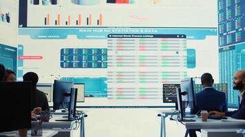 Company employees employing big data used in solving tasks, studying infographics on a huge display. Business analysts reviewing current situation numbers for annual reports. Camera B. photo