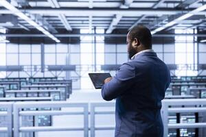 Employee in server hub using tablet to monitor energy consumption across supercomputer rigs. Admin in high tech data center making sure rackmounts are functioning optimally photo