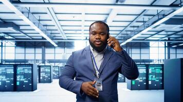 IT technician talking on phone in data center, coordinating server maintenance and troubleshooting tasks. Manager surrounded by server racks and high tech equipment in telephone call, camera B photo