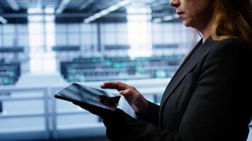 System administrator monitoring server room, doing checkup, inputting data on tablet of needed fixes. IT support employee working in data center facility housing storage rackmounts, camera B close up photo
