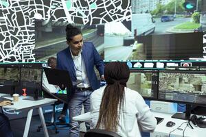 Indian man instructing his employees in using CCTV surveillance system to help couriers with directions and gps coordinates. Shipping agency working on express delivery service, satellite map. photo