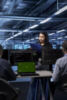 Technician inspecting server farm gear, reading paperwork from clipboard while staff members work on green screen laptop. Admins checking supercomputers with mockup notebook device photo