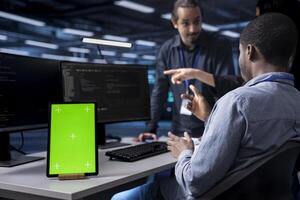 Multiethnic team using green screen tablet to oversee servers used for managing databases. Diverse staff members collaborating while working on mockup device in data center storing information photo