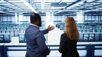 Data center engineer presenting equipment to inspector supervising operations. IT specialist in server farm doing tour for supervisor monitoring equipment performance, camera B photo