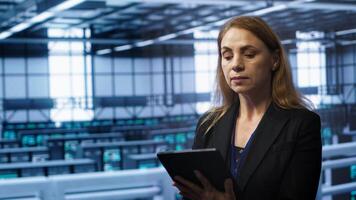 Admin in server room checks recovery plan on tablet, monitoring equipment energy consumption. IT professional uses notebook in data center workplace, ensuring rigs are functioning optimally, camera A photo