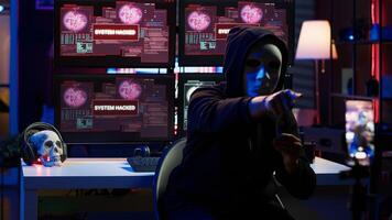 Evil programmer concealing identity using mobile phone to film ransom in secret base. Scammer with anonymous mask using cellphone to record blackmail footage, threatening victims, camera A photo