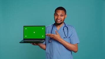 Portrait of practitioner in medical uniform showing instructions on isolated screen laptop. Healthcare professional doing presentation using mockup notebook, studio backdrop, camera B photo